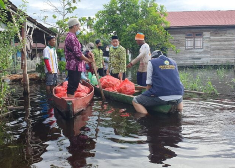 Ketua Harian DMI Kota, H.Rus'ansyah saat menyalurkan bantuan paket sembako menggunakan perahu untujk menuju rumah warga terdampak banjir. (Photo/ist)