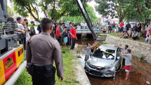 Mobil berwarna abu-abu terjun bebas ke dalam parit.