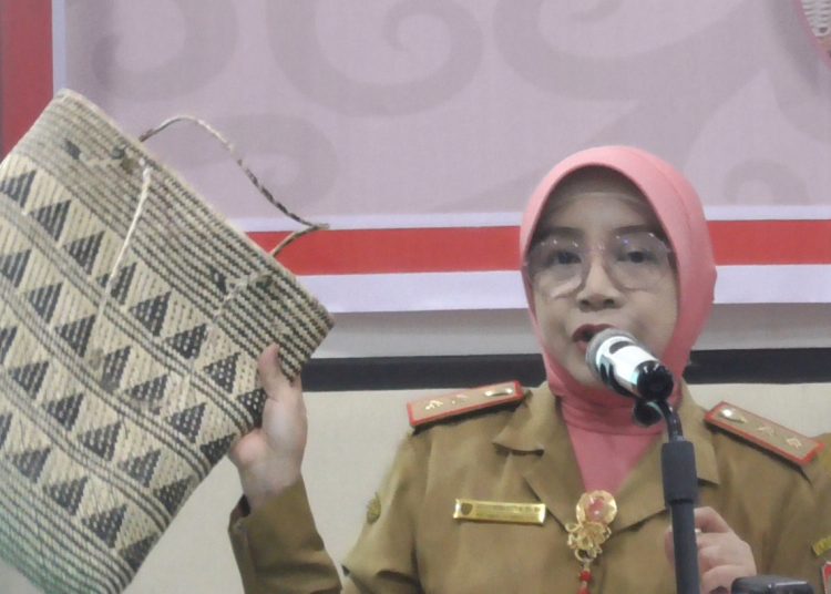 Kepala Disdagperin Prov. Kalteng Hj. Aster Bonawaty, SH, MH saat menyampaikan sambutan sambil menunjukkan sebuah tas hasil kerajinan lokal Kalteng berbahan dasar rotan. (Photo/ivan)